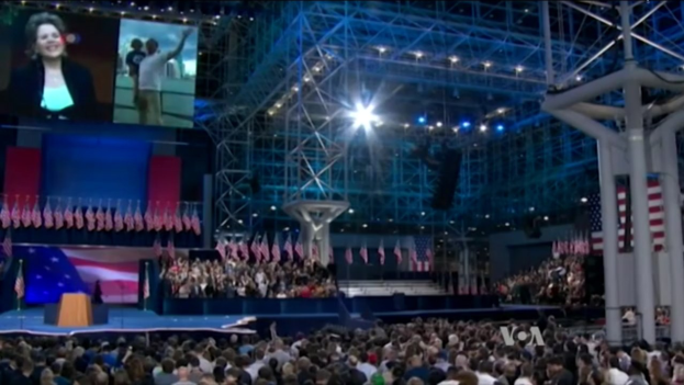 Eine große Menschenmenge sitzt vor einer Bühne mit einem Podium, Mikrofon, Fahnen, einem Bildschirm und Beleuchtungsausrüstung und wartet auf eine Präsidentschaftsdiskussion.