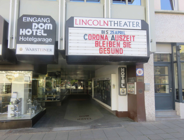 Außenansicht des Lincoln Theaters in Berlin, Deutschland, mit Glasfenstern und -türen und einer Tafel mit Text sowie einem Inneren, das voller verschiedener Gegenstände zu sein scheint.