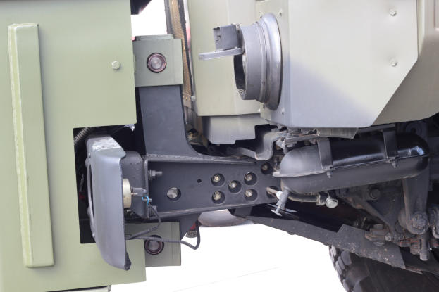 Nahaufnahme eines gepanzerten Militärfahrzeugs auf einer weißen Oberfläche, das ein Rad und eine große montierte Waffe an der Rückseite zeigt.