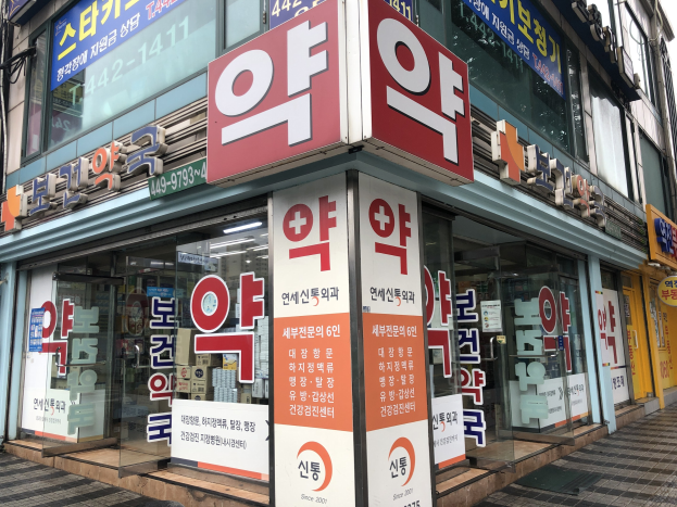 Außenansicht einer modernen Glaswand-Apotheke in Seoul, Südkorea, mit einer Tafel, auf der "Südkoreas erste Apotheke in Seoul" steht.