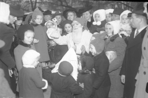 Schwarze und weiße Illustration von Santa Claus umgeben von Kindern mit Mützen, Bäumen im Hintergrund und Text unten.