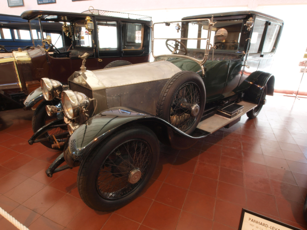 Ein Oldtimer mit einem eleganten, klassischen Design und einem glänzenden Finish, der in einem Museum ausgestellt ist, umgeben von Informationsschildern, einer Seilabsperrung und gerahmten Ausstellungsstücken an der Wand.