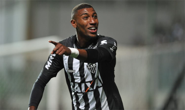 Ein Fußballspieler in einem schwarz-weißen gestreiften Trikot lächelt, während er ein Tor feiert.