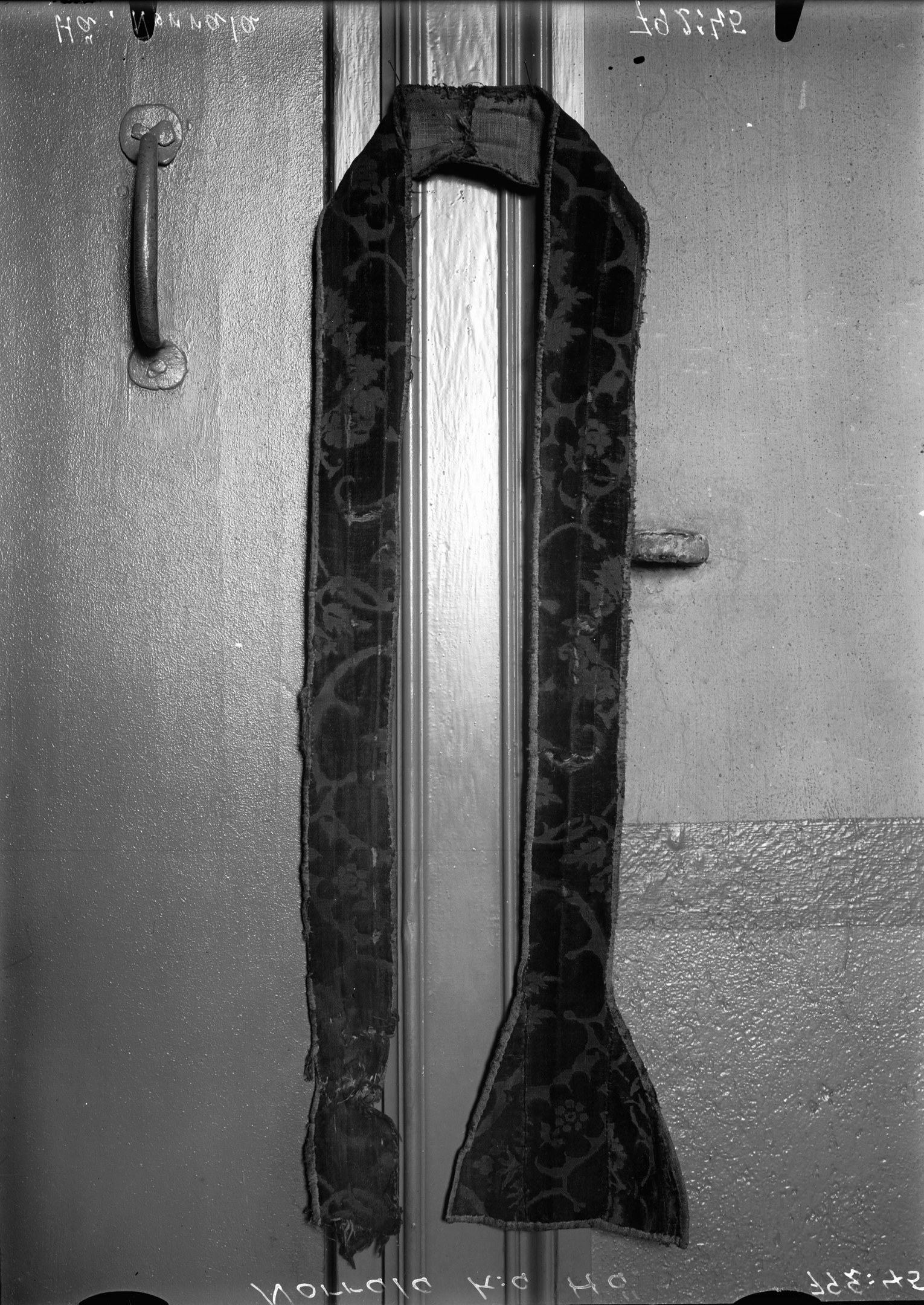 Schwarz-weißes Foto einer Tür mit Griff und einem gemusterten Tuch daran.