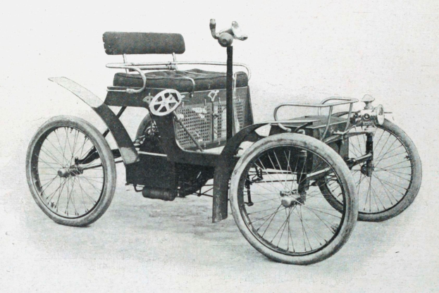Vintage-Schwarz-Weiß-Foto eines frühen 1900er-Elektroautos mit schlankem, aerodynamischem Design, großem runden Scheinwerfer, geschwungener Dachlinie, vier großen Rädern, prominentem Heckmotor, hellbezugtem Sitz und Armaturenbrett mit Knöpfen und Hebeln.