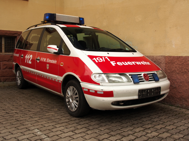 Ein roter und weißer Minivan, der als Krankenwagen gekennzeichnet ist, steht vor einem Fensterfront.