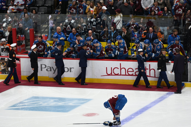 Eishockeyspieler auf dem Eis umgeben von Menschen mit Mützen und Stöcken, mit Zuschauern im Hintergrund und Tafeln mit "Colorado Avalanche vs San Jose Sharks - 3/24/15 NHL Pick, Odds, and Prediction".