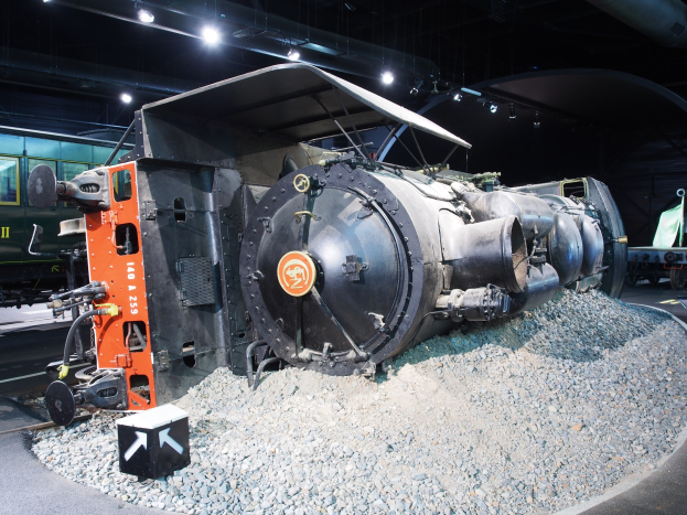 Eine alte Dampflokomotive, die in einem Museum ausgestellt ist und von Steinen umgeben ist, die von Deckenlampen beleuchtet werden.