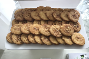 Ein weißer Teller voller Kekse steht auf einem Tisch umgeben von Gläsern und anderen Gegenständen, mit einem Papier am Boden, das Text und ein Logo anzeigt.