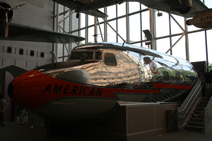 Ein Flugzeug der American Airlines wird in einem Museum ausgestellt, umgeben von Menschen, mit einer Treppe auf der rechten Seite und einem Gebäude, Bäumen und einem klaren blauen Himmel im Hintergrund.