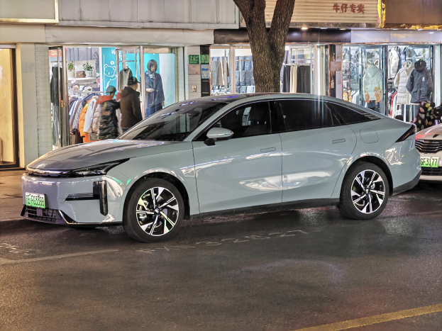 Elektrischer Mitsubishi Lancer EV auf einer nächtlichen Stadtstraße geparkt, umgeben von beleuchteten Schaufenstern, Schaufensterpuppen und Beschriftungen.