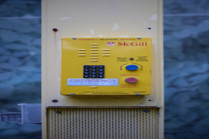 Gelber Notrufknopf an einer Gebäudewand montiert, mit Tasten und Text für Notrufe.