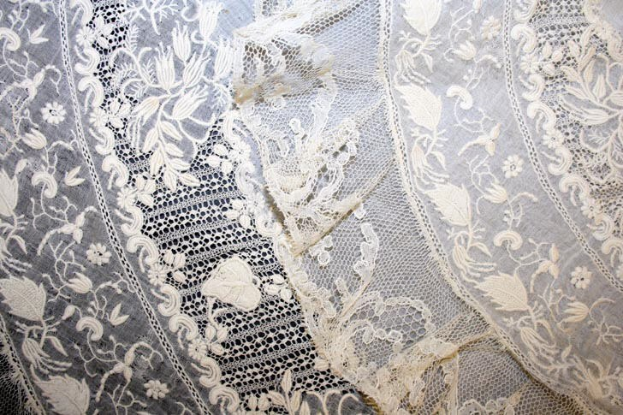 Nahaufnahme eines weißen Hochzeitskleids mit feiner, kunstvoller Spitzenverzierung in verschiedenen Mustern auf einem leichten, luftigen Stoff.