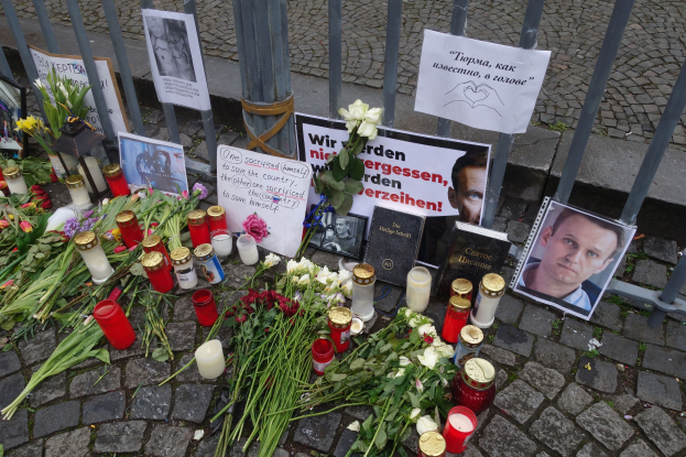 Gedenkstätte in Berlin mit Blumen, Kerzen, Fotos und Plakaten vor einem Zaun