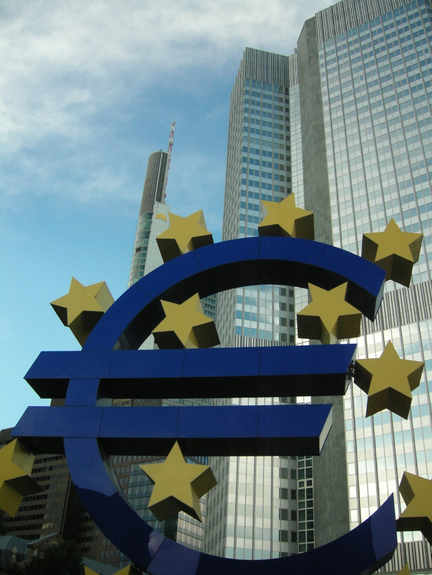 Eurozeichen vor dem Hauptsitz der Europäischen Zentralbank in Frankfurt, Deutschland, mit Bäumen und einem bewölkten Himmel.