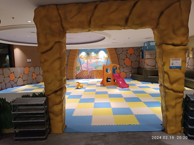 Kinderspielbereich mit einem zentralen Torbogen, Spielzeugen auf dem Boden, Regalen auf beiden Seiten, einer bemalten Wand im Hintergrund und Deckenleuchten.