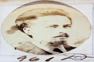 Ein altes Foto eines Mannes mit Schnurrbart und Bart, der einen Anzug und eine Krawatte trägt und direkt in die Kamera blickt.