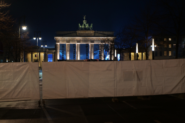 Brandenburger Tor in Berlin bei Nacht, mit einem weißen Tuch bedeckt, von Straßenlaternen beleuchtet, mit Bäumen, Gebäuden und Himmel im Hintergrund.