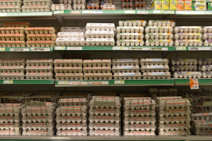 Ein Supermarktregal mit ordentlich angeordneten Eiertrays neben verschiedenen Früchten, Gemüsen und anderen Lebensmitteln.
