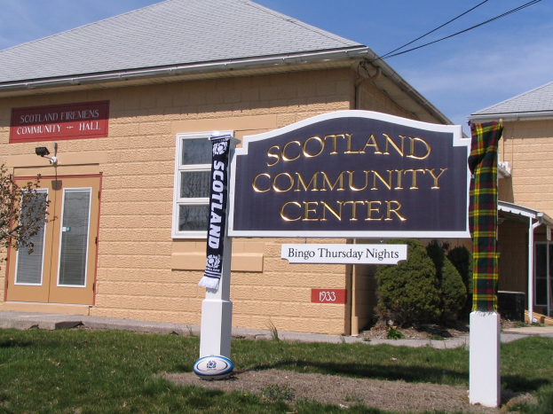 Außenansicht des Scotland Community Center mit einem Namensschild, Gras, einem Ball, Pflanzen, einem Baum, Stromleitungen und einem bewölkten Himmel.