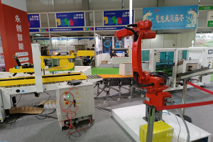 Gruppe von Robotern auf einem Tisch in einer Fabrikumgebung umgeben von Maschinen, Kabeln, Leiterplatten und Menschen im Hintergrund.