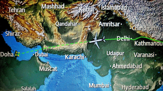 Eine Weltkarte mit einem Flugzeug, das von Delhi nach Karachi fliegt und die Flugroute über Land und Wasser zeigt.