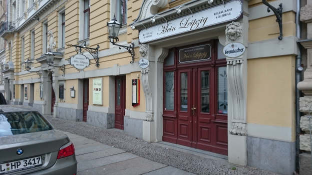 Ein Auto, das auf einer Straße neben einem Gebäude mit Fenstern, Türen, Schildern, Lampen und anderen Gegenständen geparkt ist, mit einem sichtbaren Kfz-Kennzeichen.