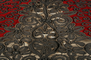 Nahaufnahme eines roten Kleids mit schwarzer Litzen-Überlagerung, das detaillierte Litzen-Muster auf rotem Stoff zeigt.