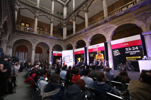 Eine Gruppe von Menschen, die an einem Tisch mit einem Podium und einem Mikrofon vor einer Menge, Kameras und Bannern sitzen, was eine Pressekonferenz für das CDMX 2017-Ereignis vermuten lässt.