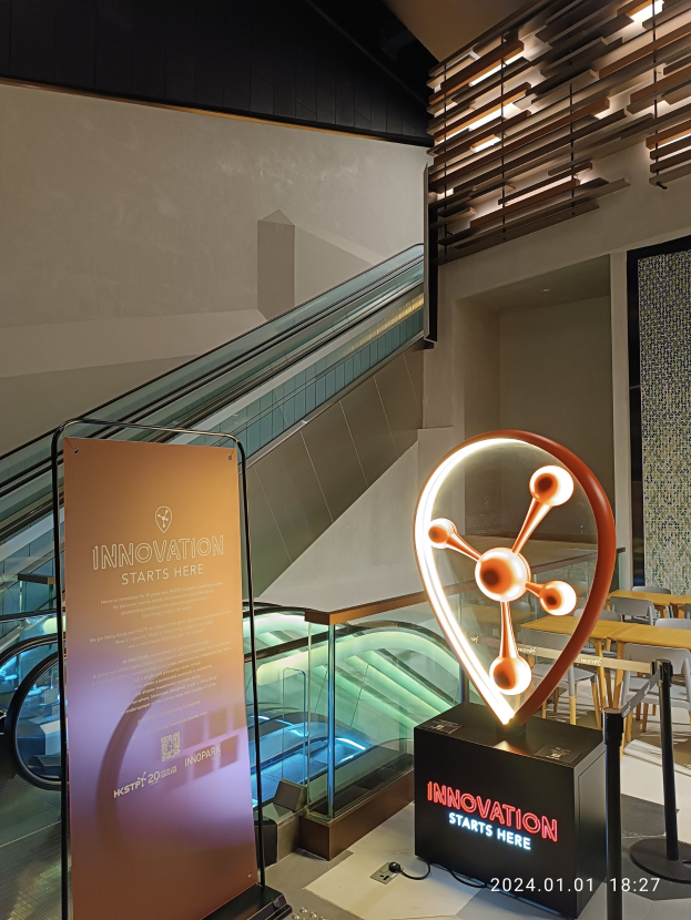Großes Schild in einem Gebäude mit einer Rolltreppe im Hintergrund, mit Tischen und Stühlen auf der rechten Seite und einer Tafel mit "Innovation Starts Here" auf der linken Seite, was auf die HSTP20 Expo hinweist.