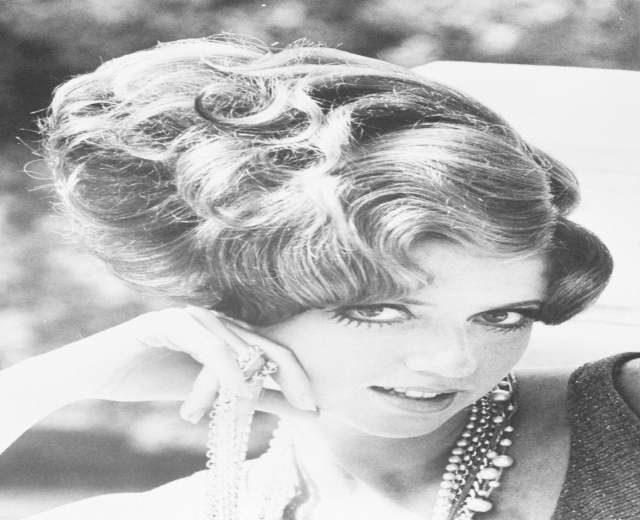 Schwarzes und weißes Foto von Prinzessin Diana in einem Kleid und Schmuck mit einem unscharfen Hintergrund.