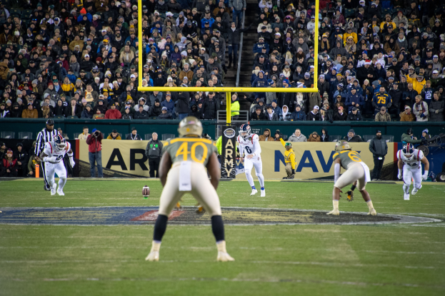 Fußballspieler in Helmen und Uniformen konkurrieren auf einem Feld mit Zuschauern auf den Tribünen und Stadionwerbung im Hintergrund.