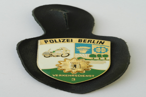 Ein schildförmiges Polizeibadgebnis mit der Aufschrift 'Polizei Berlin' auf blauem Hintergrund, weißer Umrandung und einem zentralen weißen Stern, das auf einer Oberfläche platziert ist.