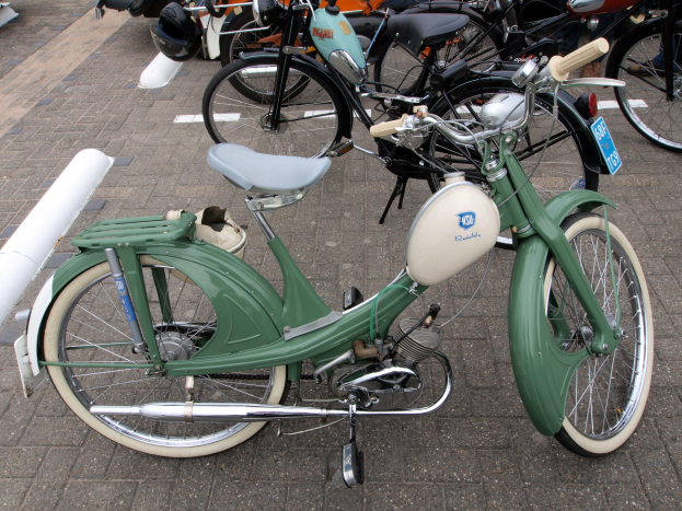 Ein grünes Moped mit weißem Rahmen und schwarzem Sitz neben anderen Motorrädern auf einem Gehweg geparkt, umgeben von ein paar Menschen.