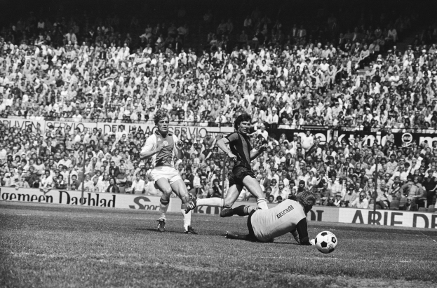Schwarzes Foto von Fußballspielern im Einsatz auf einem Feld mit Zuschauern im Hintergrund und einer "Bundesliga 1978-79 Ajax 1-1 Hannover 96"-Tafel.