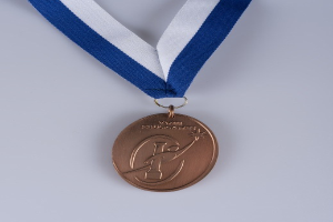Goldmedaille mit blau-weißem Band auf weißem Hintergrund, mit eingravierter Inschrift.