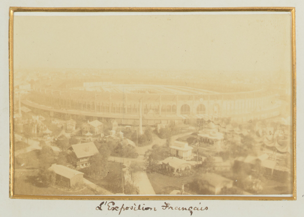 Altes Schwarz-Weiß-Foto eines Stadions, umgeben von Gebäuden, Bäumen und Strommasten, mit Text unten.