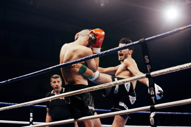 Zwei Boxer kämpfen in einem hell erleuchteten Ring mit einem Schiedsrichter im Hintergrund.
