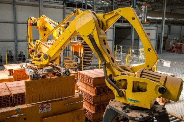 Großes industrielles Lager mit gestapelten Kisten, Überkopfkrane, Zaun, Pfosten und einer fernen Wand in einer Fertigungsumgebung.