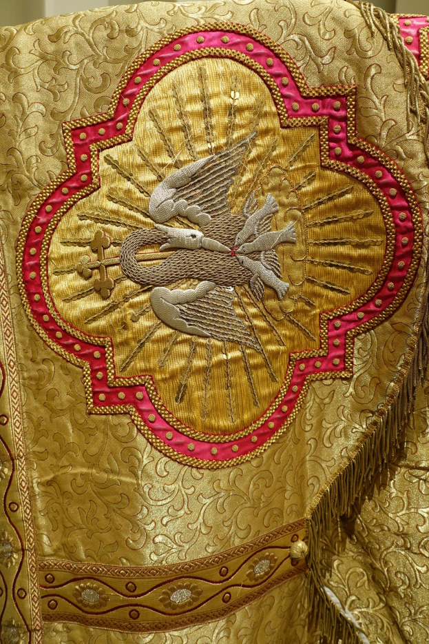 Nahaufnahme eines Priestergewandes mit aufwendiger Gold- und Rotstickerei und luxuriösem, königlich anmutendem Design vor einem neutralen Wandhintergrund.