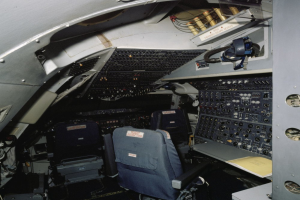 Ein Flugzeugcockpit mit zwei Sitzen, einem Tisch mit einem Buch und verschiedenen elektronischen Geräten und Kabeln.