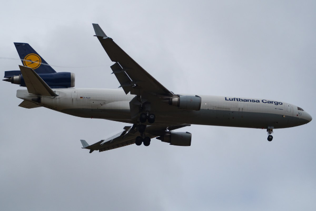 Ein Lufthansa Cargo Boeing 777-300ER im Flug, mit ausgefahrenen Flügeln und laufenden Triebwerken, mit sichtbarem Text auf dem Rumpf gegen einen bewölkten Himmel.
