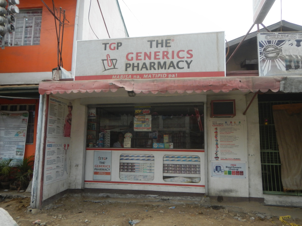 Außenansicht der "The Generics Pharmacy" Filiale mit umliegenden städtischen Elementen unter einem klaren blauen Himmel.