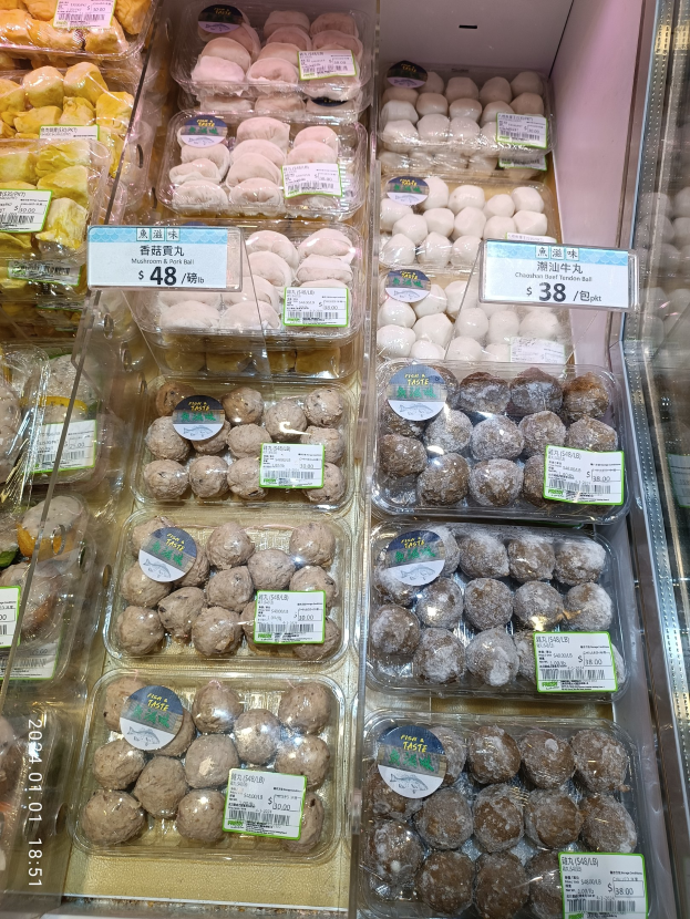 Vitrine voller verschiedener Gebäcke in Plastikboxen mit Preisetiketten, darunter Macarons und Cookies.