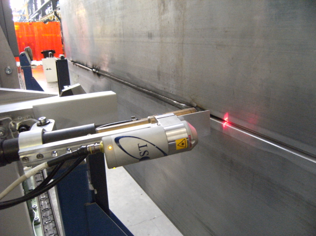 Heller Laserstrahl aus einer Schneidemaschine in einer Fabrik, der die Umgebung beleuchtet, mit einer Wand auf der rechten Seite und Gegenständen im Hintergrund.