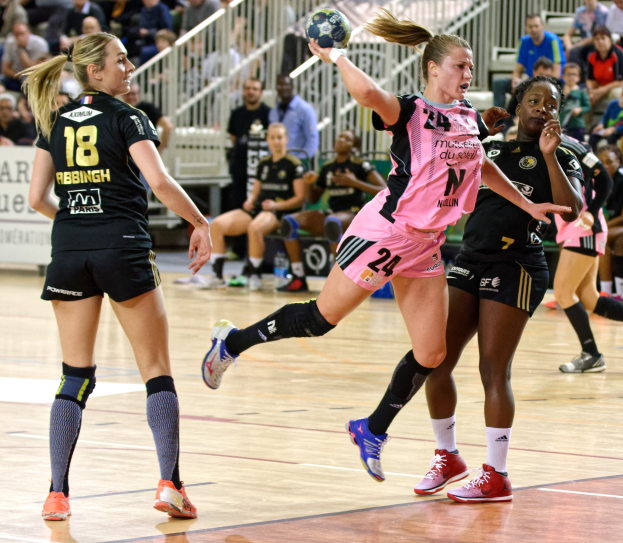 Eine Gruppe von Frauen spielt Handball auf einem Feld mit Zuschauern im Hintergrund.