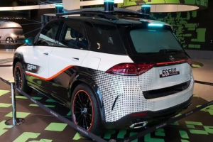 Mercedes-Benz E-Klasse Electric SUV auf der IAA in Frankfurt präsentiert, umgeben von Absperrgittern mit Seilen und Lichtern, mit einem weiteren Fahrzeug und einer textbedruckten Wand im Hintergrund.