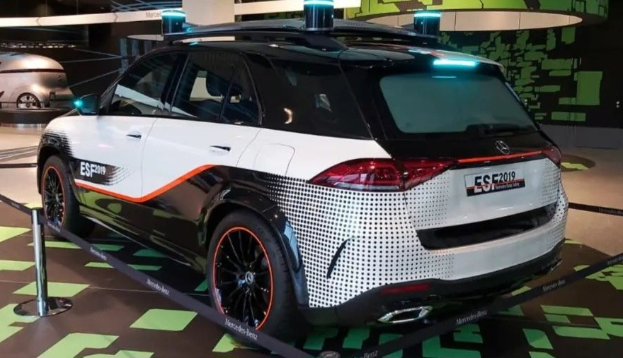 Mercedes-Benz E-Klasse Electric SUV auf der IAA in Frankfurt präsentiert, umgeben von Absperrgittern mit Seilen und Lichtern, mit einem weiteren Fahrzeug und einer textbedruckten Wand im Hintergrund.