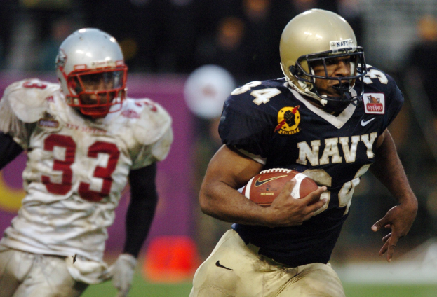 Ein Fußballspieler in einem marineblauen Trikot und Helm rennt mit dem Ball während eines Spiels, Hintergrund durch Bewegung unscharf.