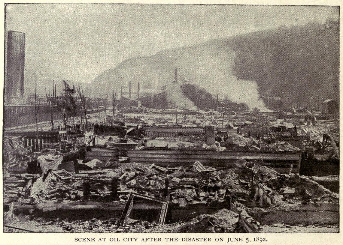 Schwarzes und weißes Foto einer Stadt nach einer Katastrophe am 5. Juni 1892, das beschädigte Gebäude, Strommasten, Rauch und einen Hügel im Hintergrund zeigt.